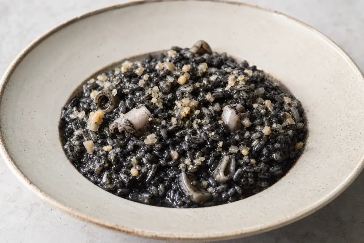 Plated black risotto garnished with cuttlefish, squid ink, and herbs.