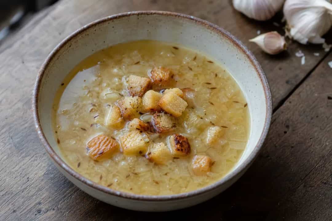 A bowl of Czech garlic soup topped with golden croutons and fresh herbs in a rustic setting.
