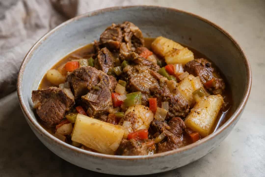 A hearty bowl of goat stew with tender yuca, herbs, and spices, garnished and steaming.