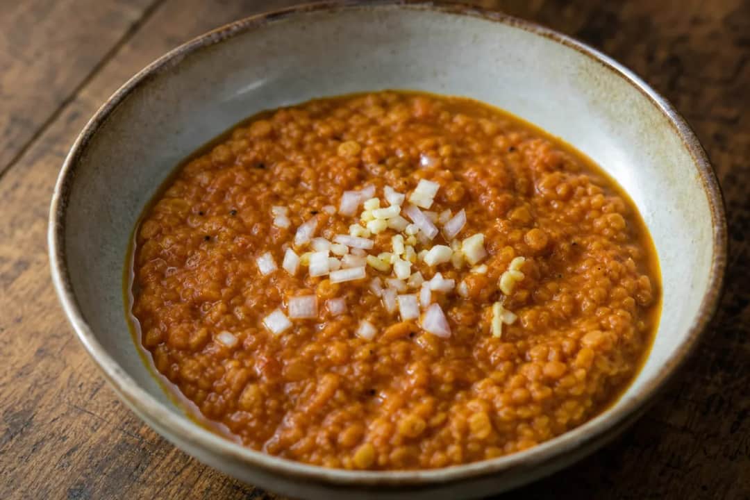 Steamy red lentil stew with a rich texture, garnished with herbs and served in a bowl.