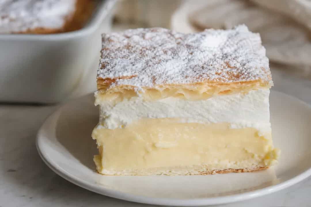 Layered Bled cream cake topped with powdered sugar, showcasing creamy custard and light pastry.