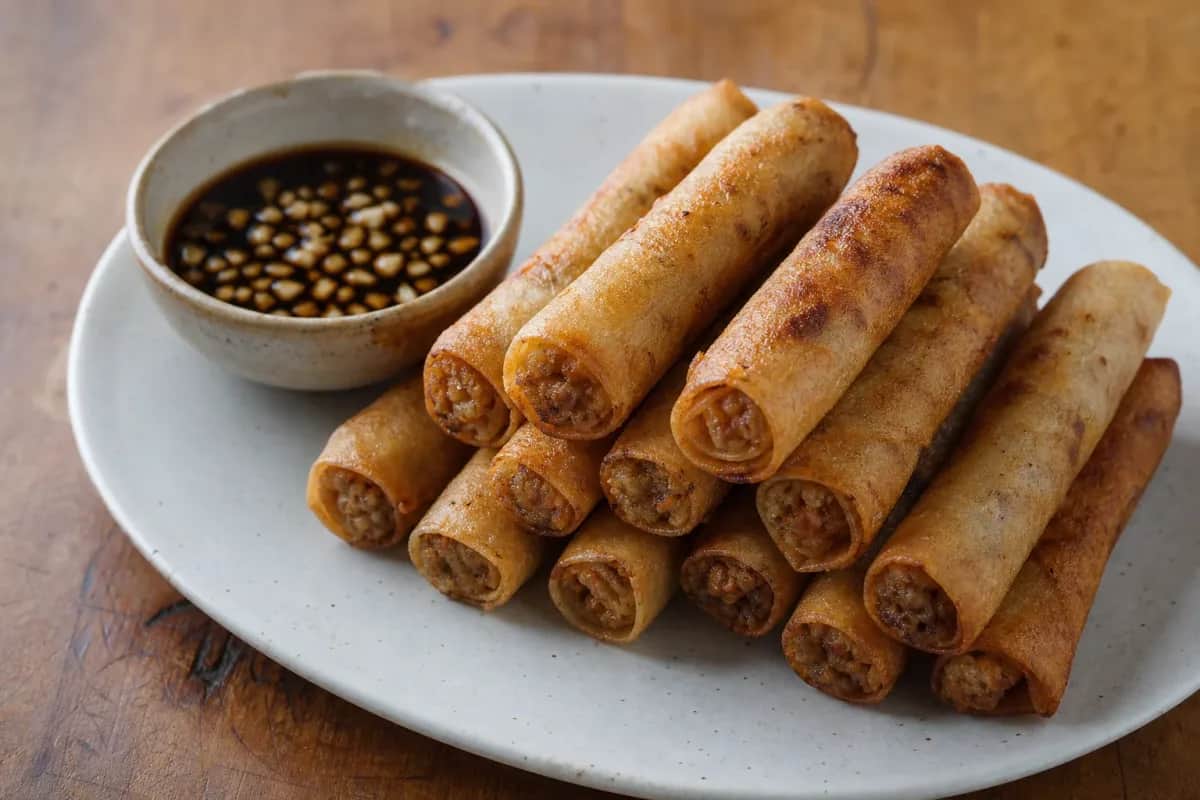 Crispy lumpiang shanghai spring rolls plated with a side of dipping sauce.