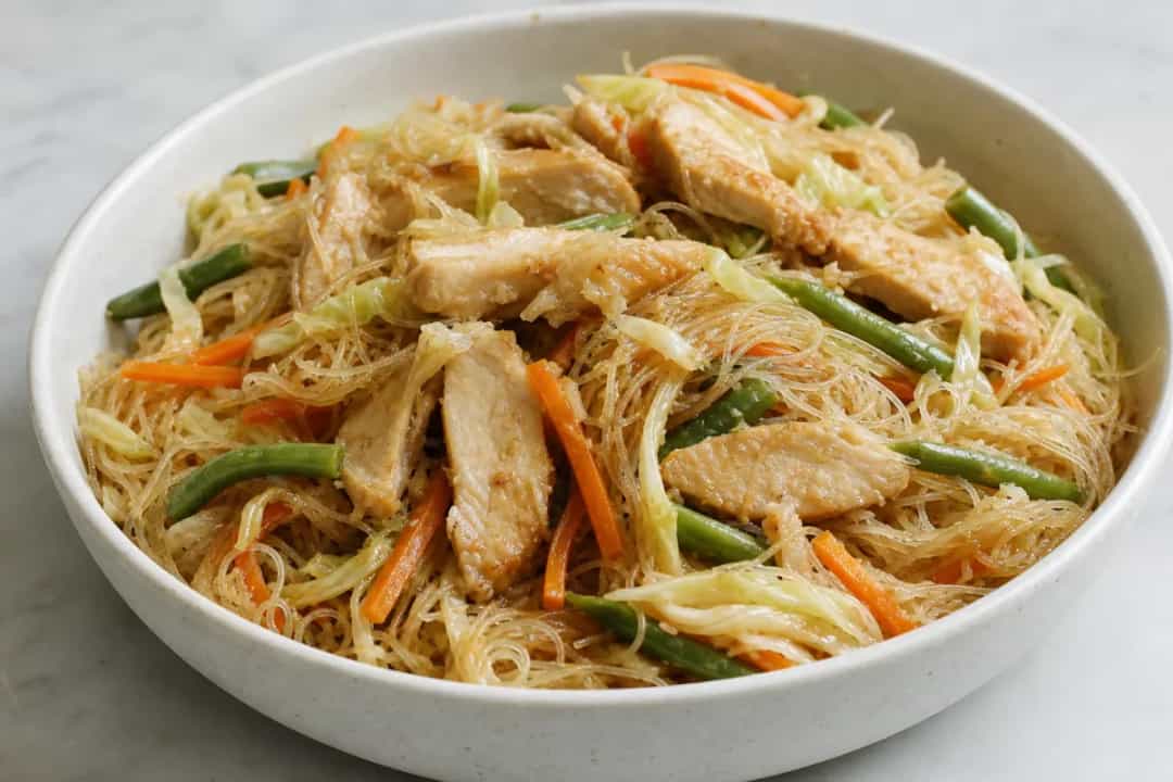 Stir-fried rice noodles topped with chicken and vibrant vegetables, garnished with green onions.