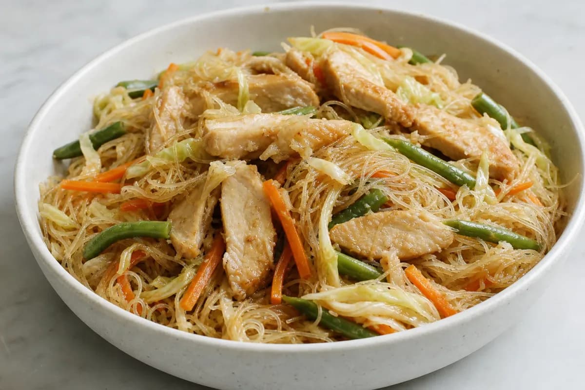 Stir-fried rice noodles topped with chicken and vibrant vegetables, garnished with green onions.
