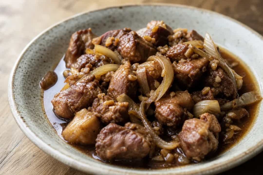 Tender pork adobo served with bay leaves and black pepper, garnished for presentation.