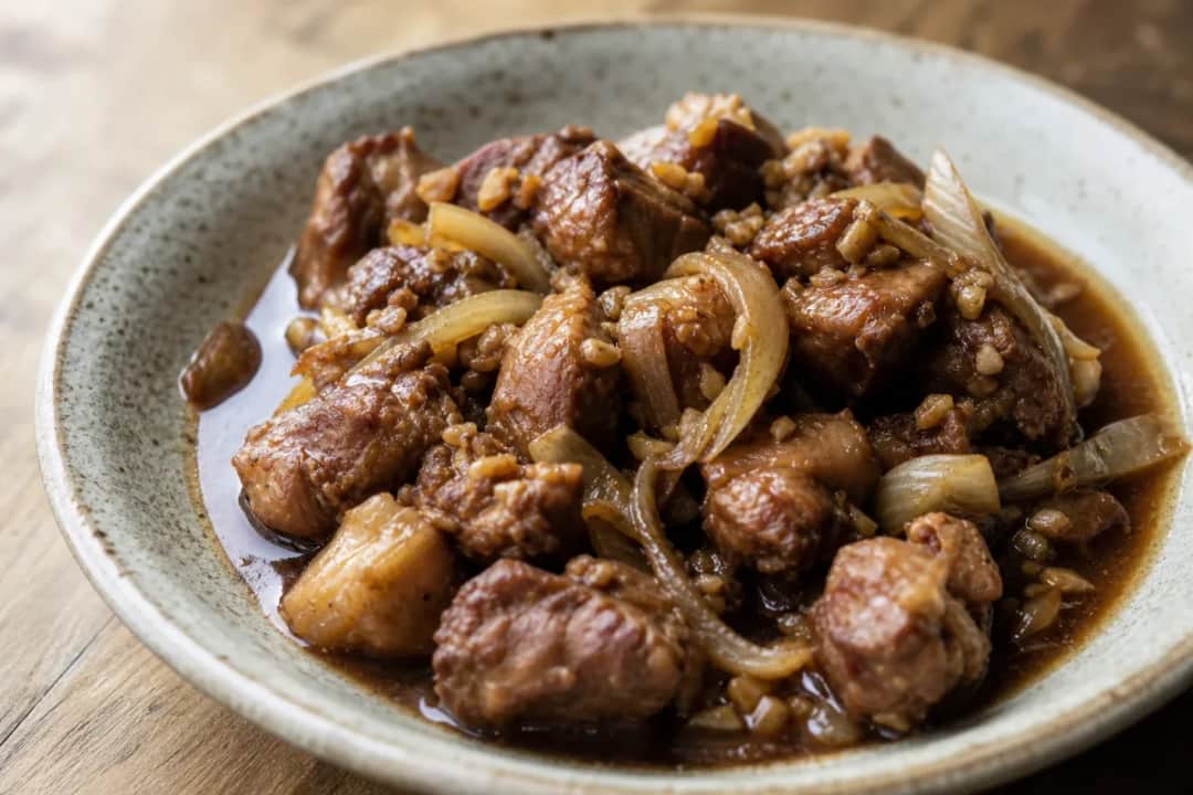 Tender pork adobo served with bay leaves and black pepper, garnished for presentation.
