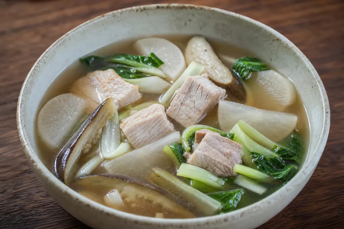 A bowl of sinigang soup featuring tender pork, vibrant vegetables, and a tangy broth, garnished with fresh herbs.
