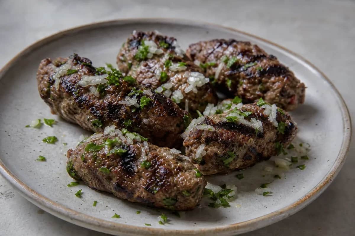 Grilled kafta kebabs garnished with herbs and served with tahini sauce.