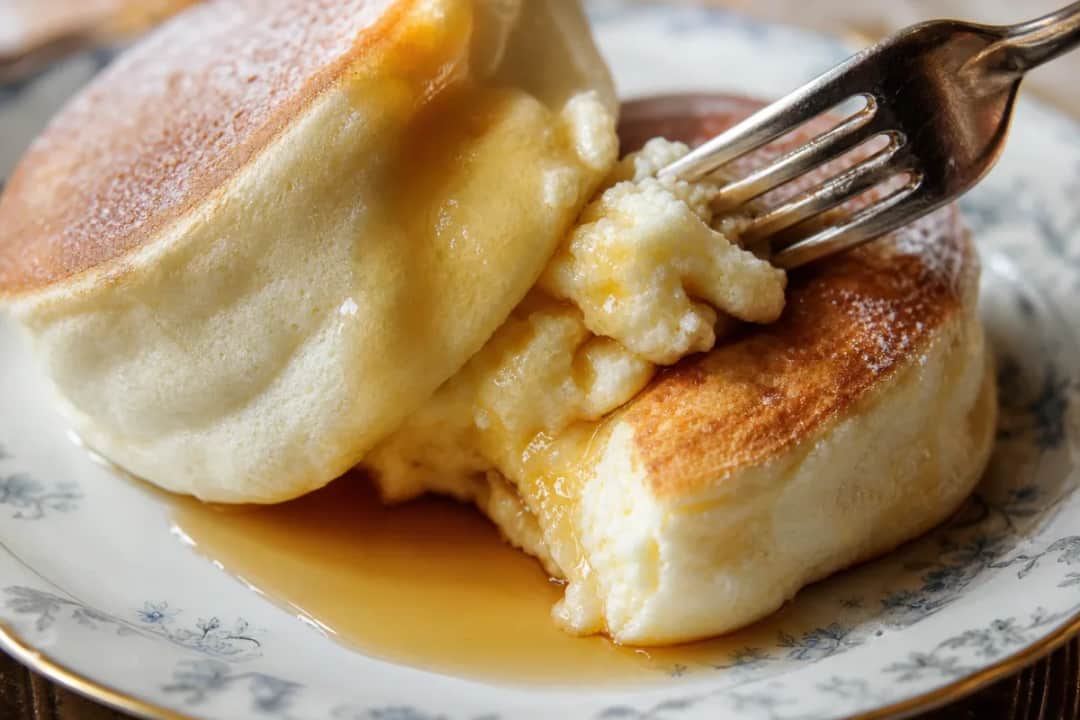 Fluffy Japanese soufflé pancakes drizzled with light maple syrup, served with whipped cream and berries.