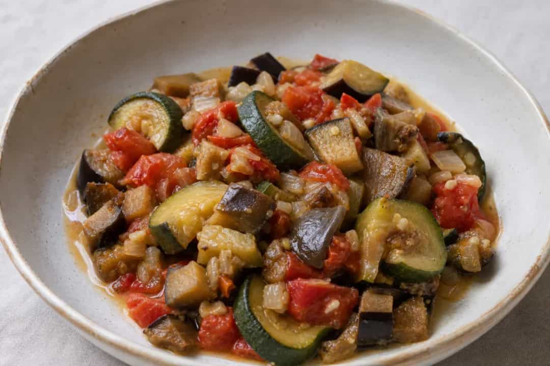 Colorful ratatouille featuring layered zucchini, eggplant, and tomatoes with a glossy finish and fresh herbs.