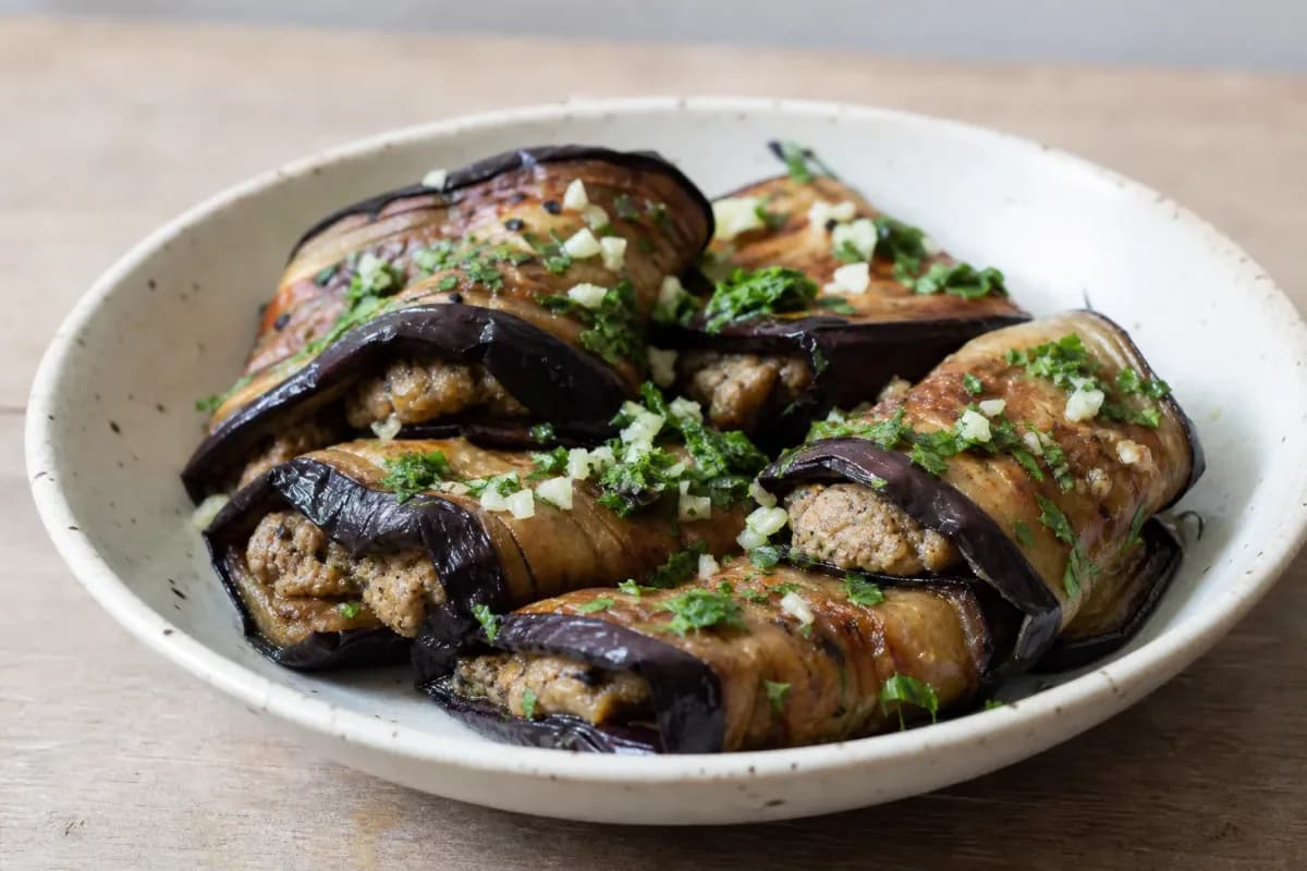 Elegant presentation of eggplant rolls filled with walnut paste, garnished with herbs.