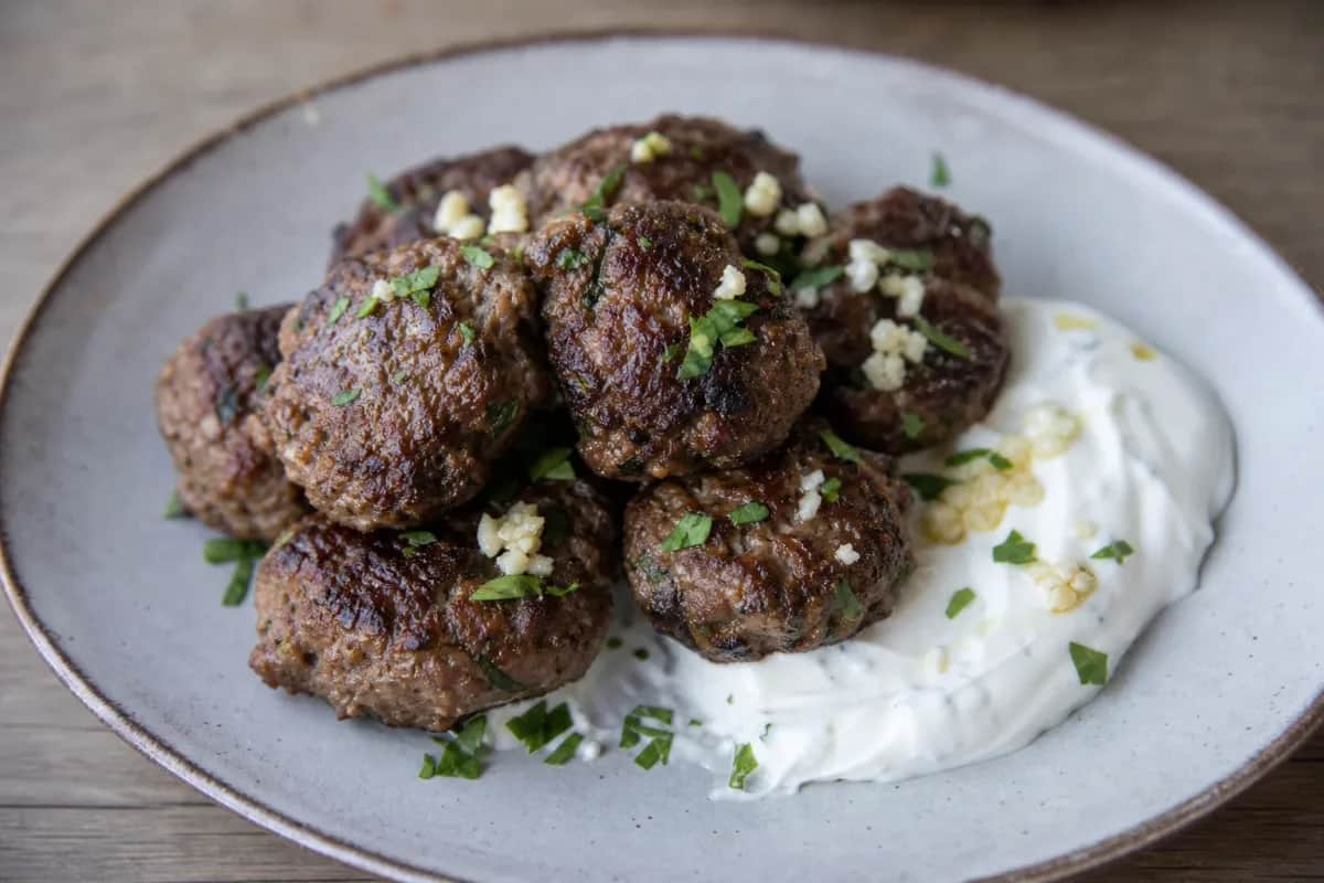 Crispy Greek keftedes garnished with herbs, served with garlic yogurt sauce on the side.