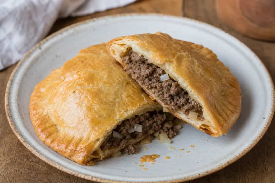 Golden-brown Haitian Pâté pastries filled with spiced ground meat, garnished with herbs.