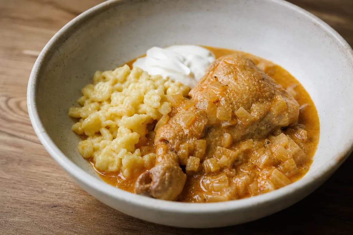 Creamy chicken paprikash with vibrant paprika sauce and soft nokedli dumplings, garnished with parsley.