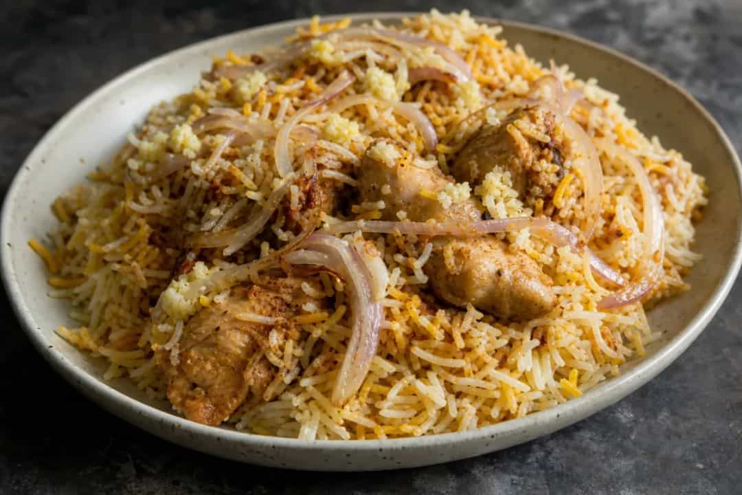 A vibrant plate of Hyderabadi chicken biryani with saffron rice, garnished with fried onions and fresh herbs.