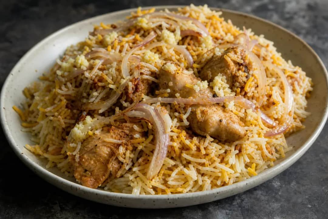 A vibrant plate of Hyderabadi chicken biryani with saffron rice, garnished with fried onions and fresh herbs.