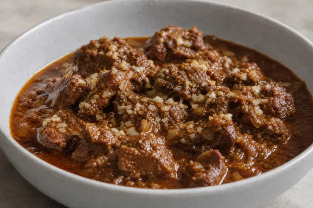 A bowl of Indian Lamb Rogan Josh garnished with fresh coriander and served with rice, showcasing tender lamb and rich red sauce.