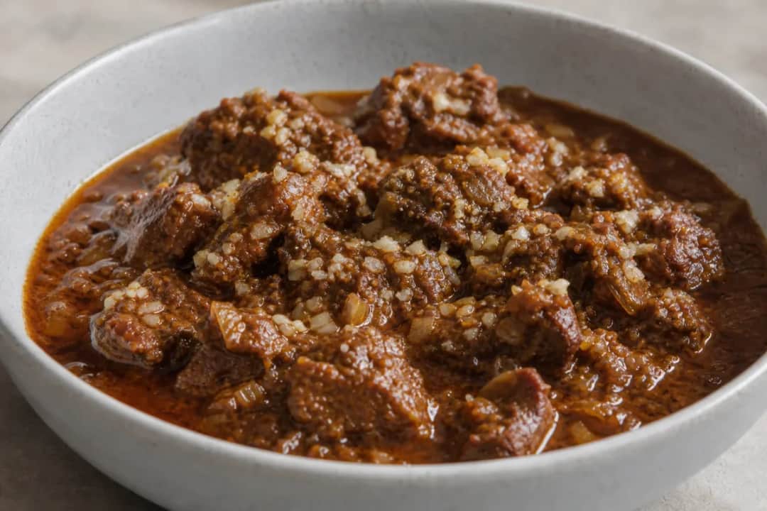 A bowl of Indian Lamb Rogan Josh garnished with fresh coriander and served with rice, showcasing tender lamb and rich red sauce.