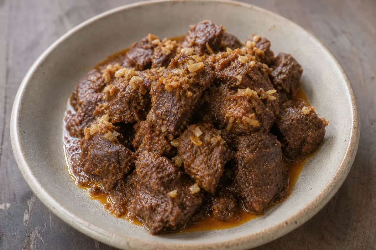 Tender beef rendang in rich coconut sauce garnished with herbs, served on a plate.