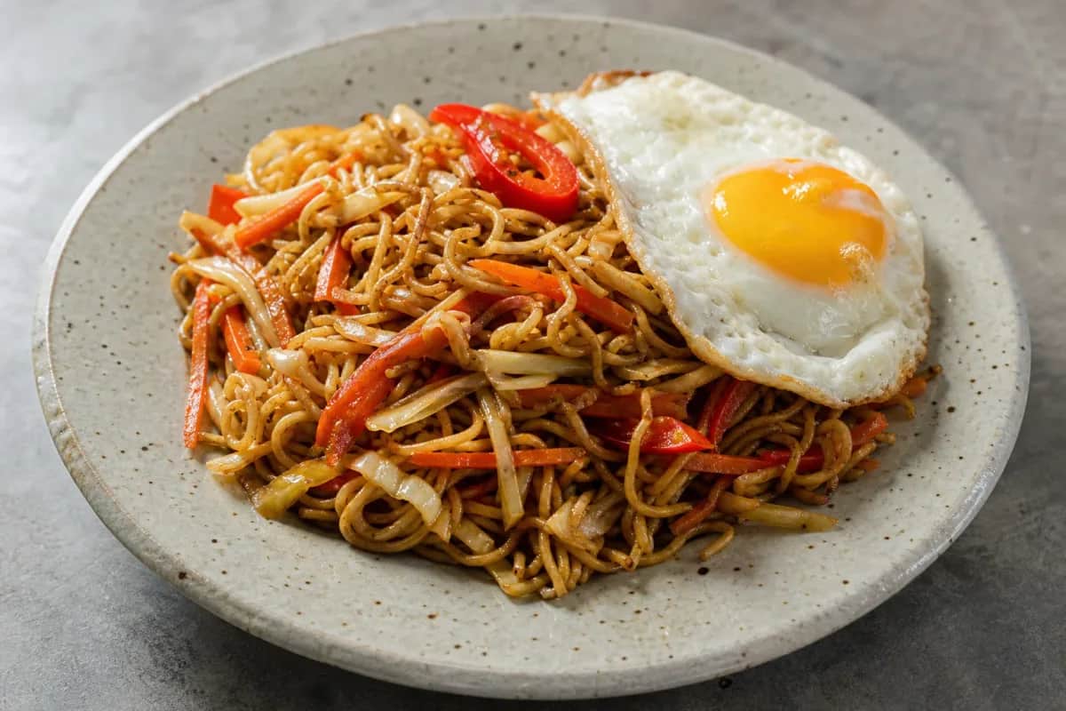 A vibrant plate of Indonesian Mie Goreng with colorful vegetables and a perfectly fried egg on top.