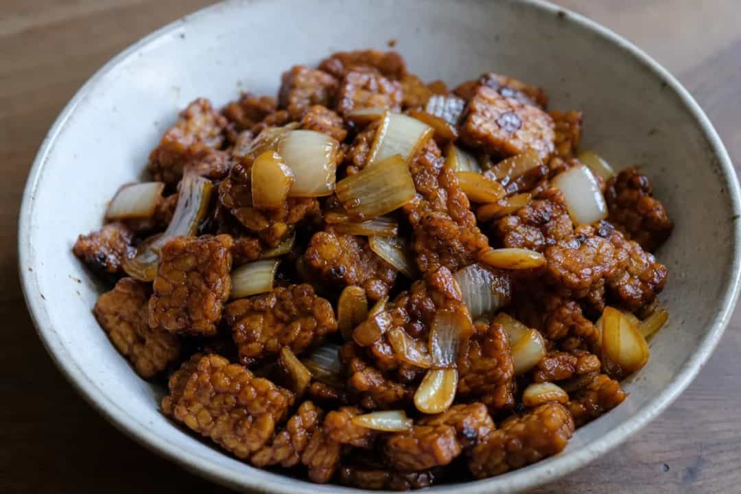 Plated Indonesian Tempeh Sambal with vibrant red chili and garnished herbs, showcasing texture and colors.