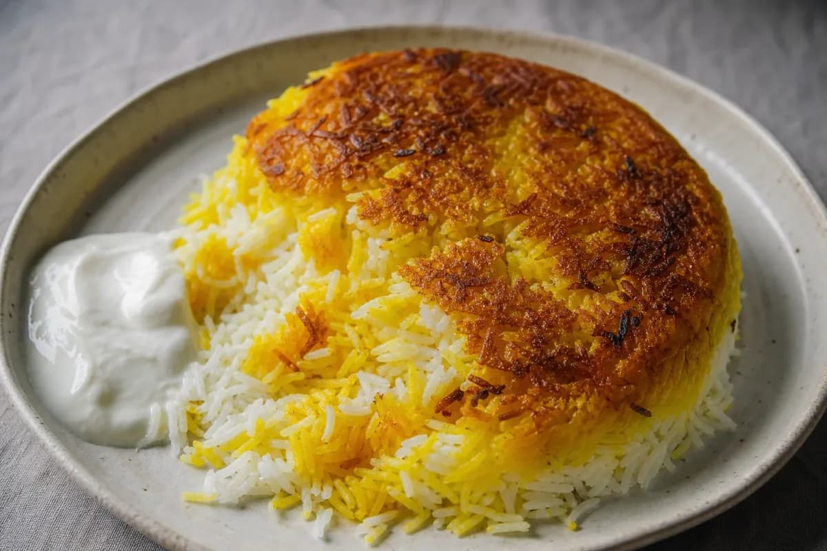 A plate of golden crispy tahdig with saffron rice, garnished with herbs and served with yogurt.