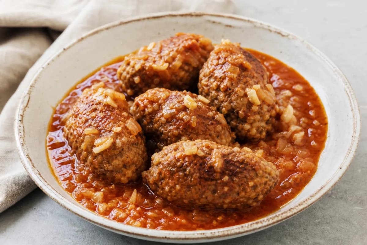 Plated Iraqi Kubba with beef and bulgur, garnished with herbs and tomatoes, showcasing a rich sauce and textures.