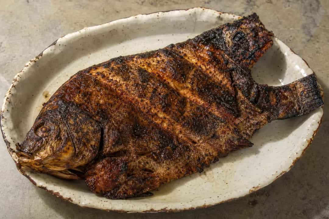 Grilled fish served with tamarind sauce, garnished with spices and herbs.