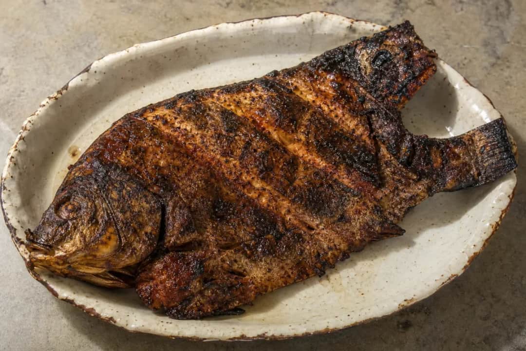 Grilled fish served with tamarind sauce, garnished with spices and herbs.
