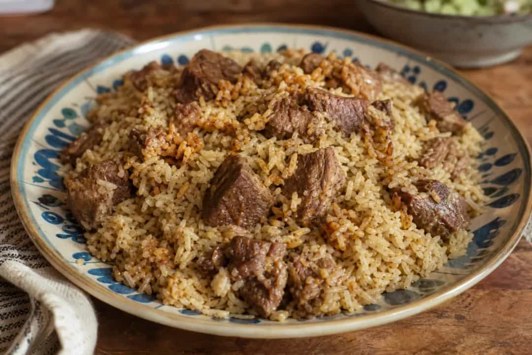 Plated Iraqi Quzi featuring tender lamb, fragrant rice, and colorful nuts and raisins garnished attractively.