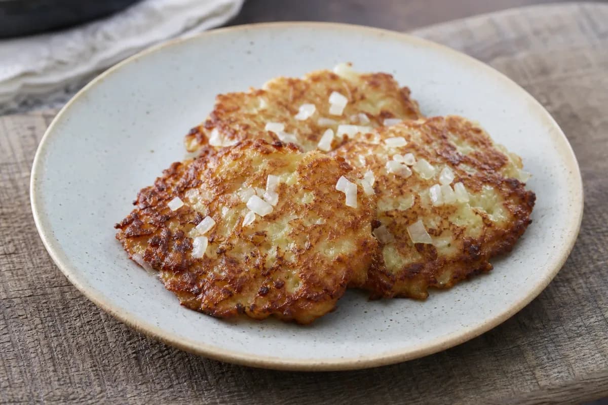 Golden-brown potato pancakes garnished with fresh herbs and served on a plate.