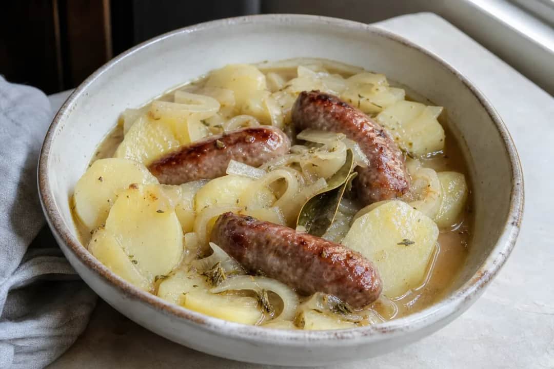 A hearty bowl of Dublin Coddle with golden sausages, tender potatoes, and onions, garnished with parsley.