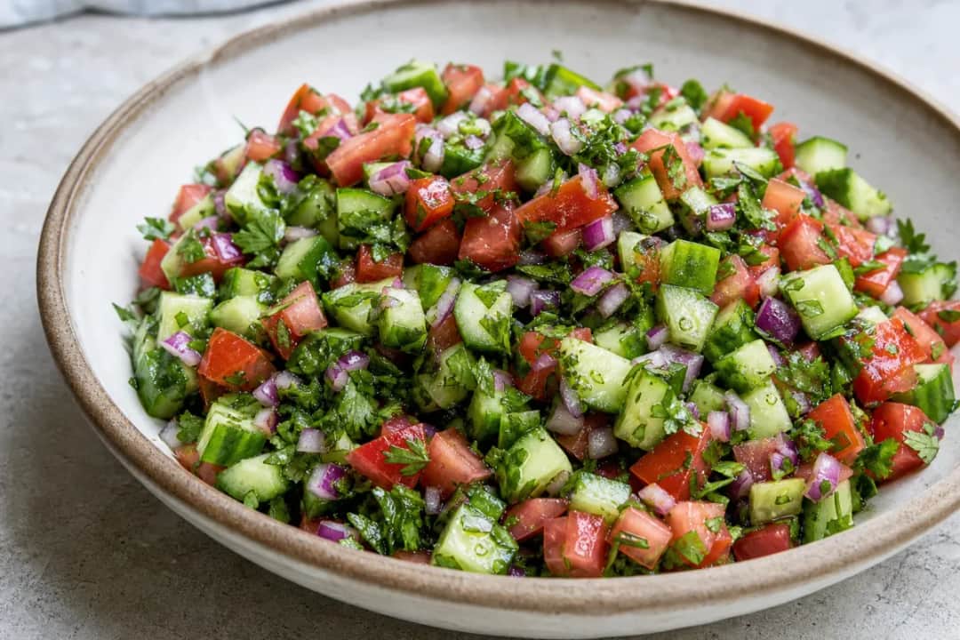 Colorful chopped salad with diced cucumbers, tomatoes, and herbs in a bowl.