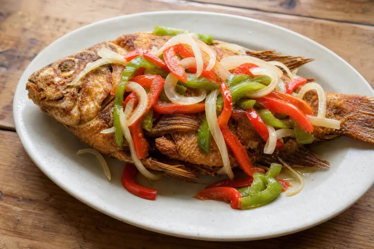 Crispy fried fish topped with colorful pickled vegetables and herbs, garnished beautifully.