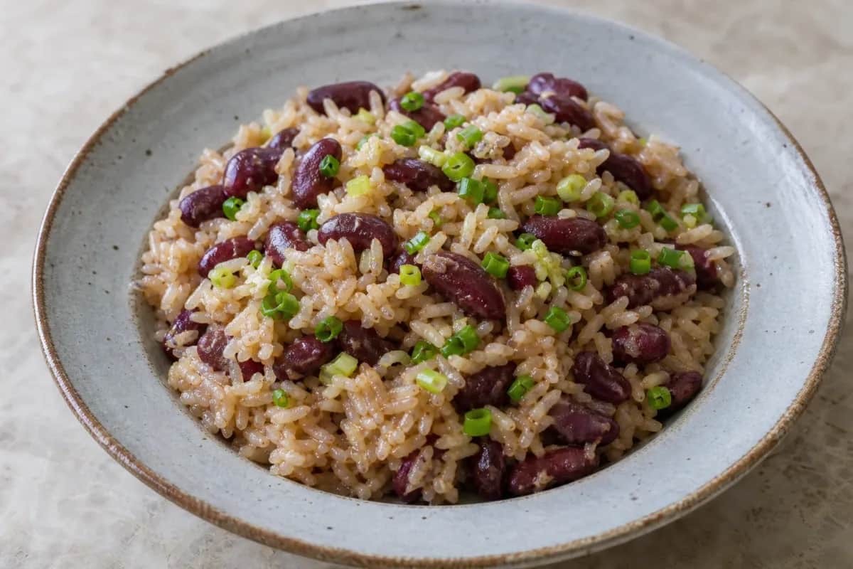 Fluffy rice mixed with red kidney beans, coconut milk, and fresh herbs garnished on a plate.