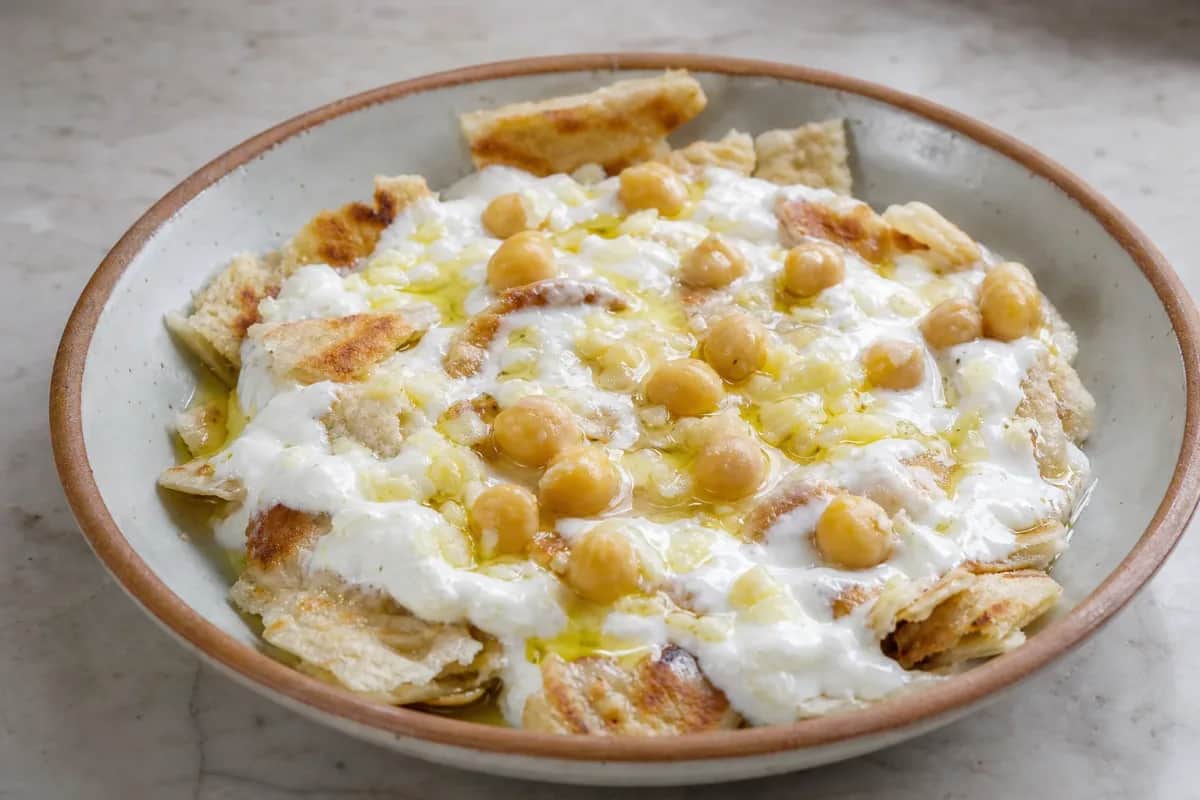 Layered dish of Fattet Hummus with creamy yogurt, chickpeas, and crispy pita on top.