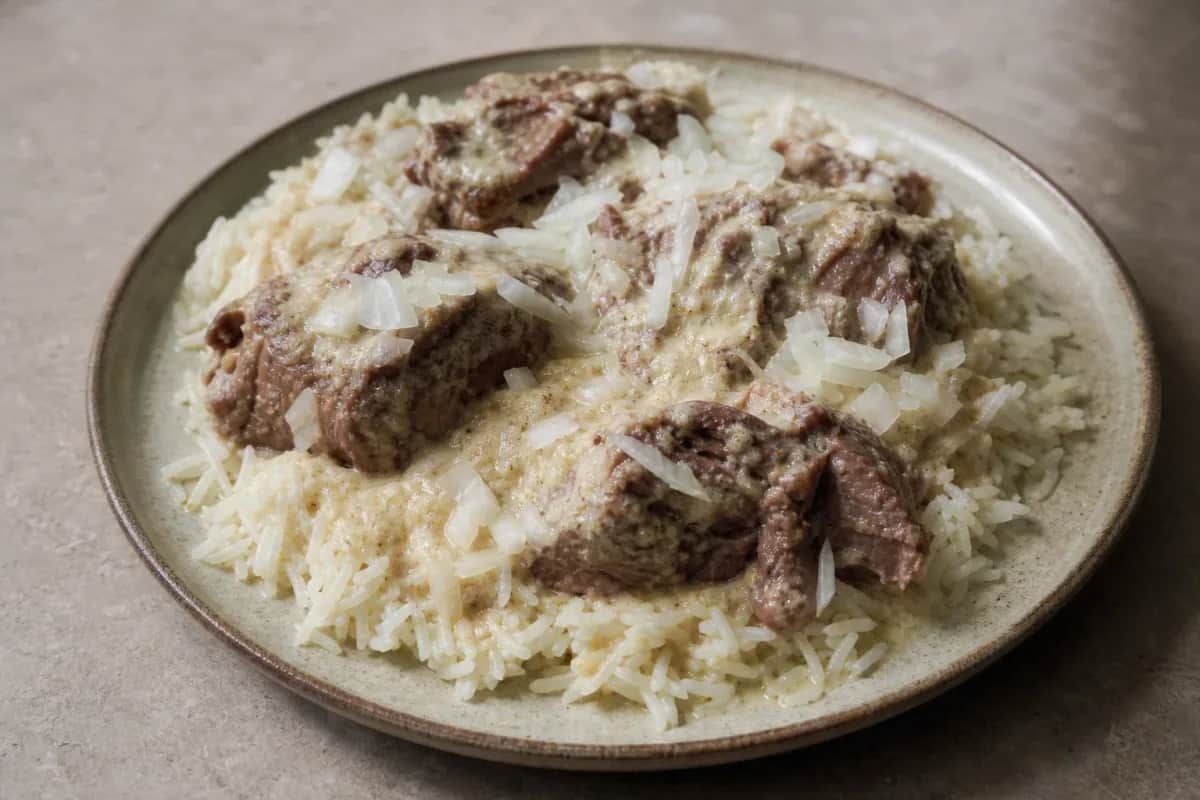 Plated mansaf featuring tender lamb, creamy jameed sauce, and fluffy rice garnished with almonds and parsley.