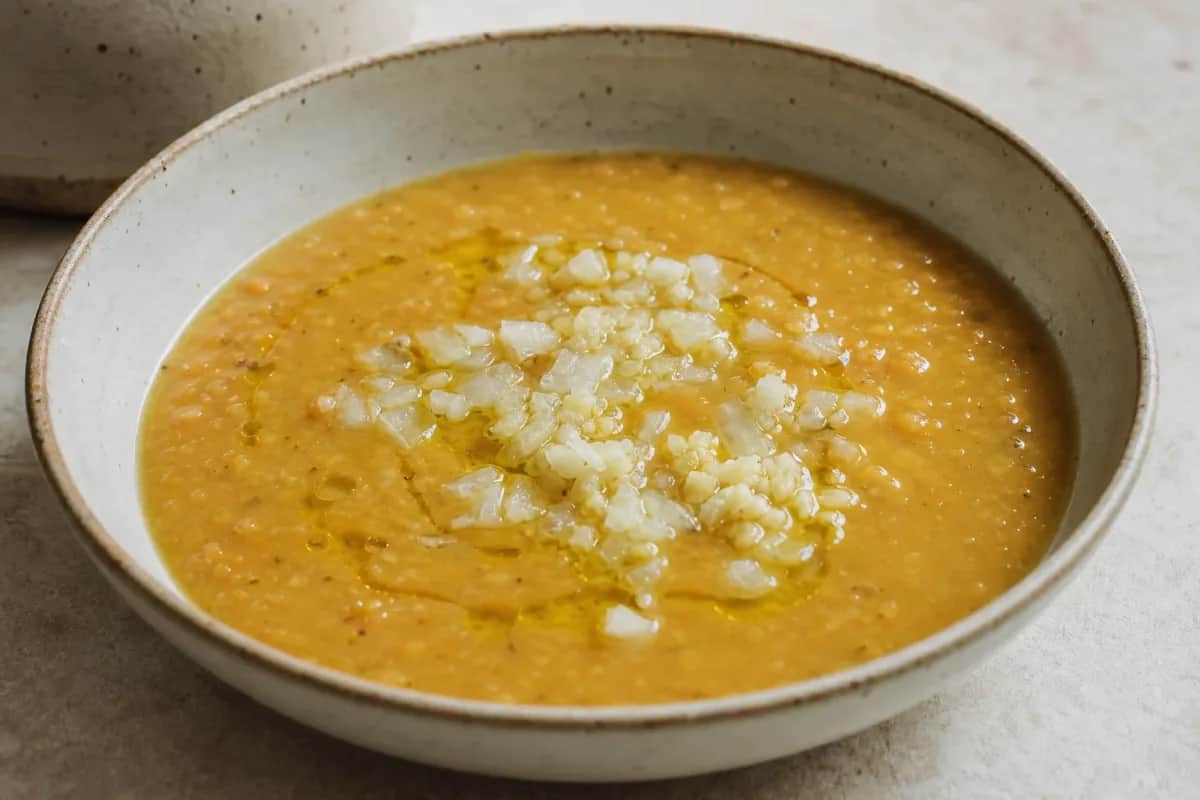 Bowl of Jordanian lentil soup garnished with lemon slices and parsley, showcasing a vibrant orange color and smooth texture.