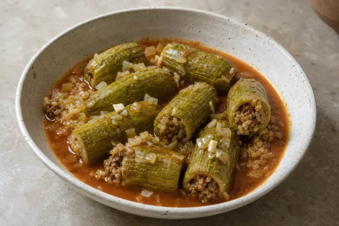 Plated Kousa Mahshi showcasing stuffed zucchini in rich tomato broth, garnished with herbs.