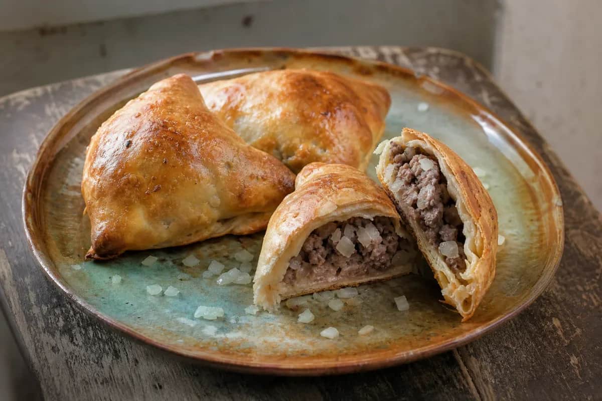 Golden-brown samsa pastries filled with tender beef, garnished with sesame seeds, served on a rustic plate.