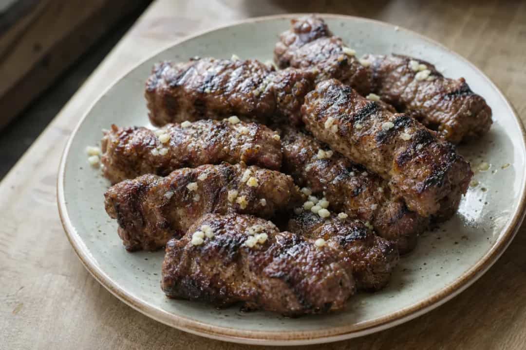Grilled mici served on a plate, garnished with fresh herbs and onions.