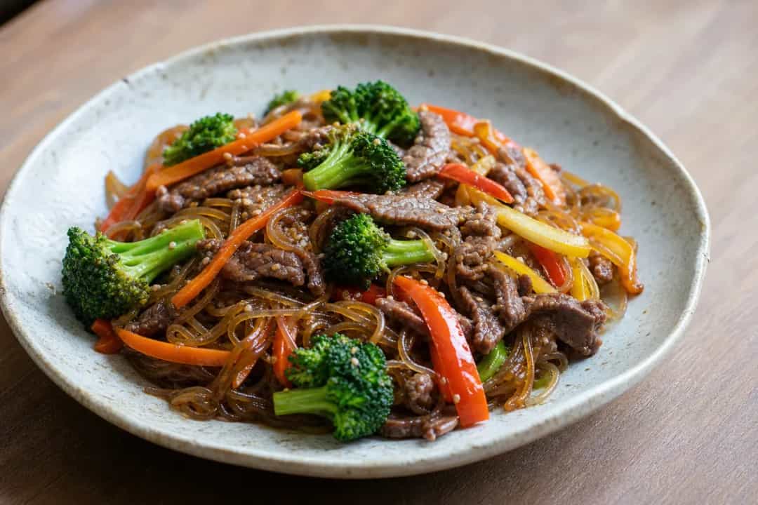 Colorful stir-fried glass noodles with beef and assorted vegetables on a plate.