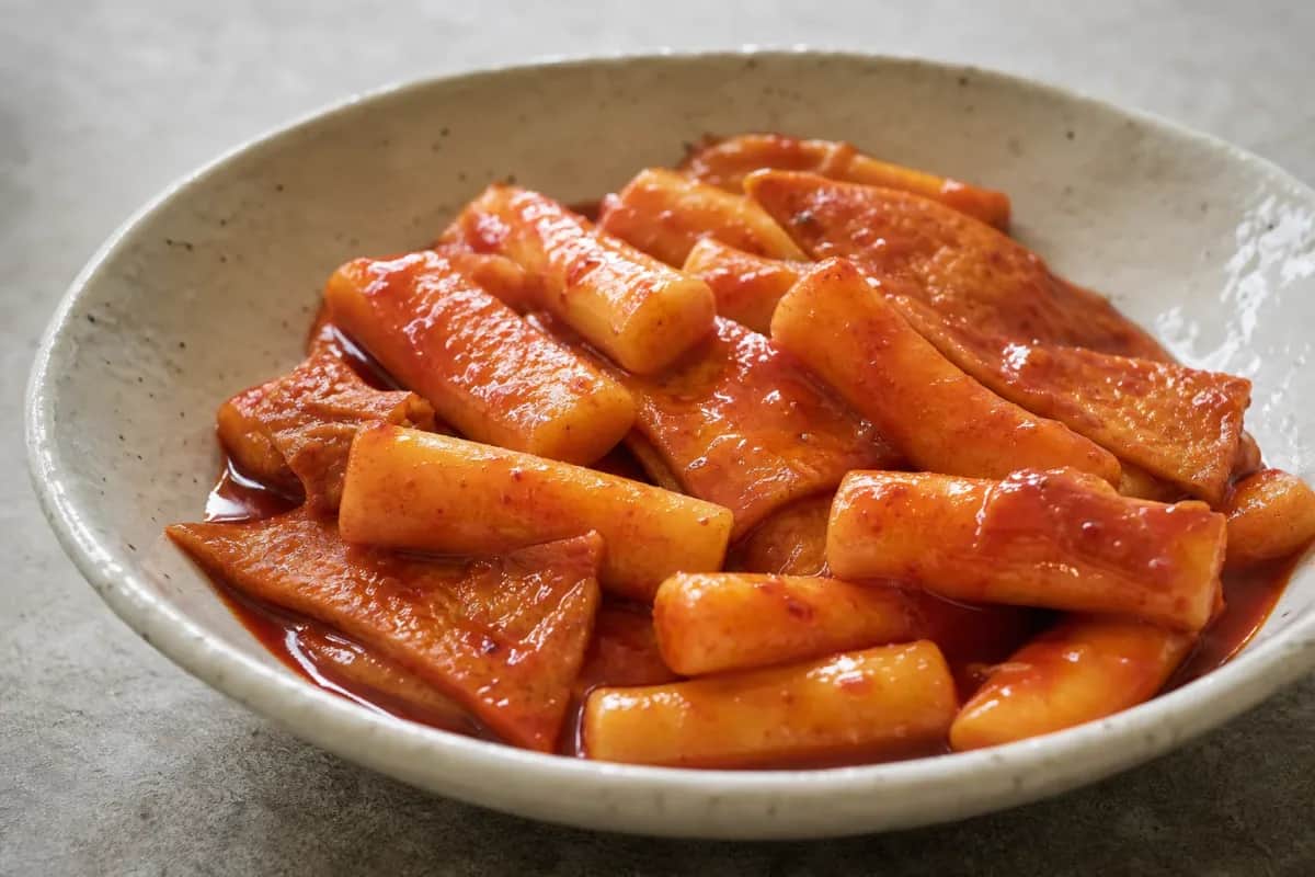 Plated tteokbokki with chewy rice cakes, fish cakes, and vibrant red sauce, garnished with scallions.
