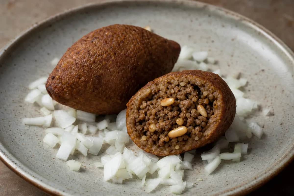 Golden-brown kubba stuffed with spiced beef, garnished with herbs and served on a plate.
