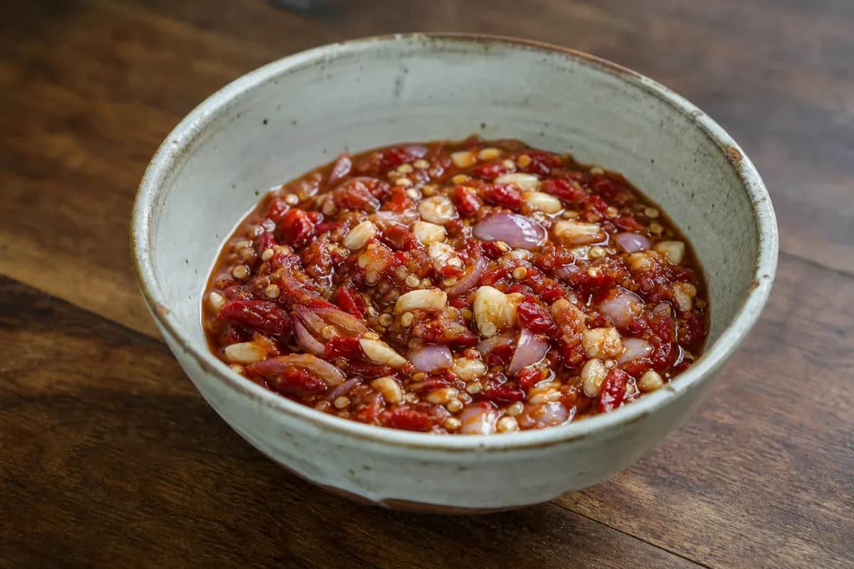 A vibrant bowl of spicy chili dip featuring minced garlic and herbs, served with fresh vegetable sticks.