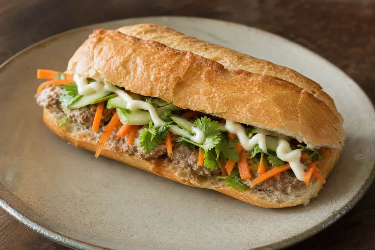 Crispy baguette filled with pâté, fresh vegetables, and herbs, sliced for serving.