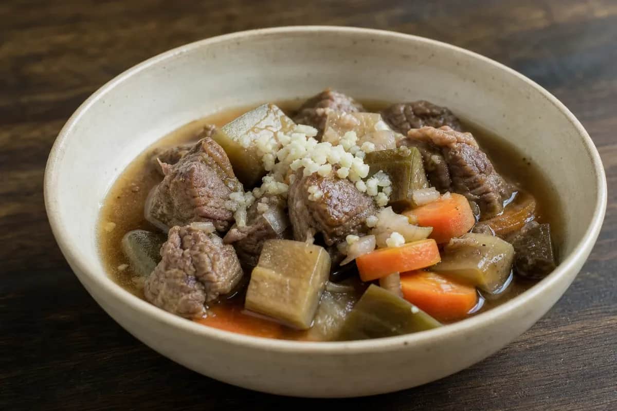 A hearty bowl of Laotian Or Lam filled with tender beef, vibrant vegetables, and fresh herbs, garnished for presentation.