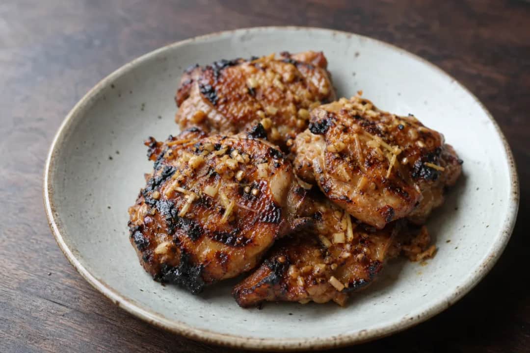 Plated Laotian Ping Gai showcasing grilled chicken, lemongrass, and herbs with a charred texture.