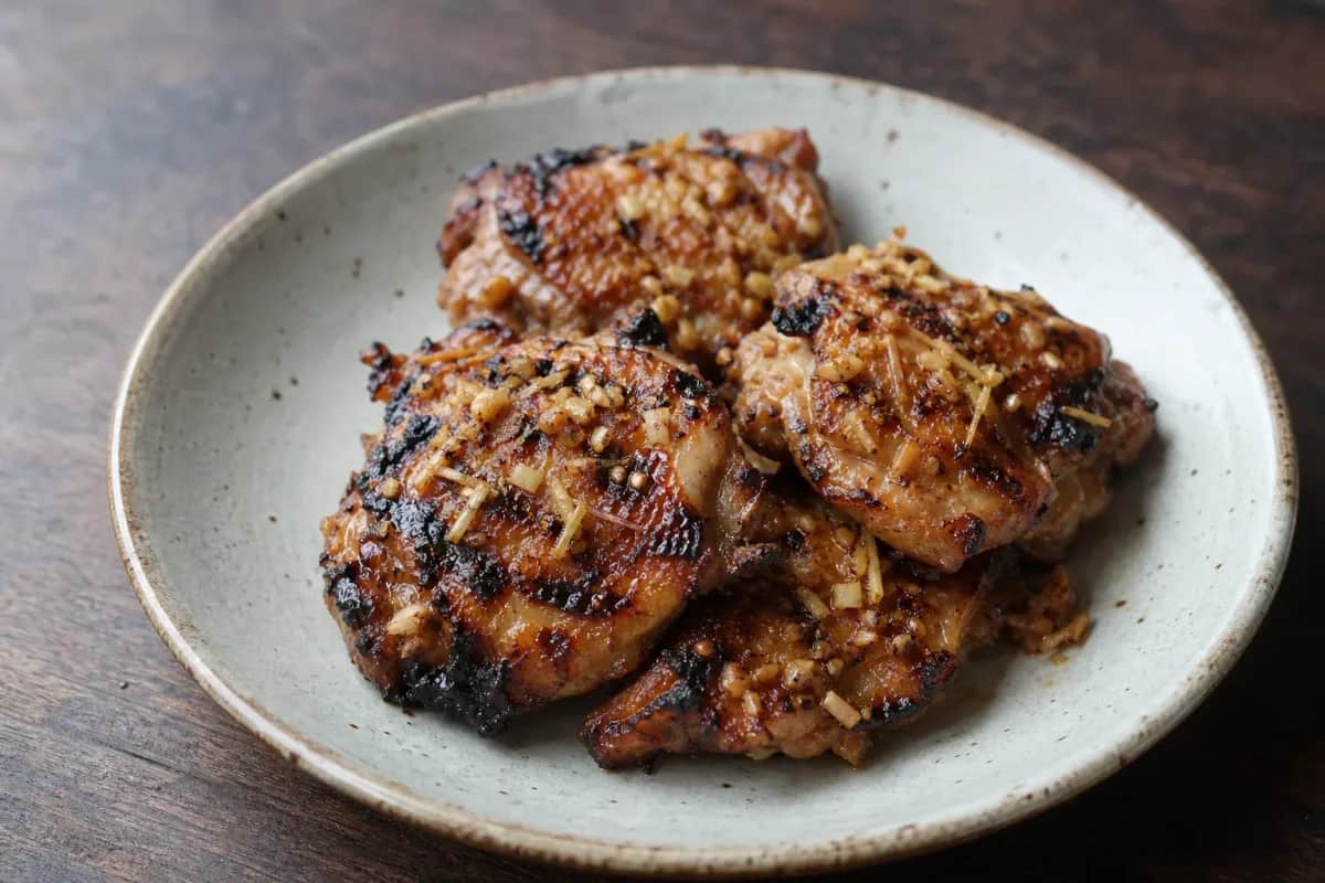 Plated Laotian Ping Gai showcasing grilled chicken, lemongrass, and herbs with a charred texture.