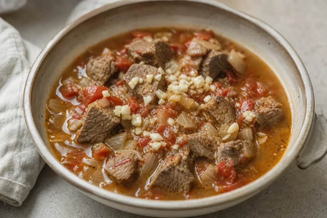 A bowl of Libyan shorba filled with tender lamb, ripe tomatoes, and aromatic spices, garnished with fresh herbs.